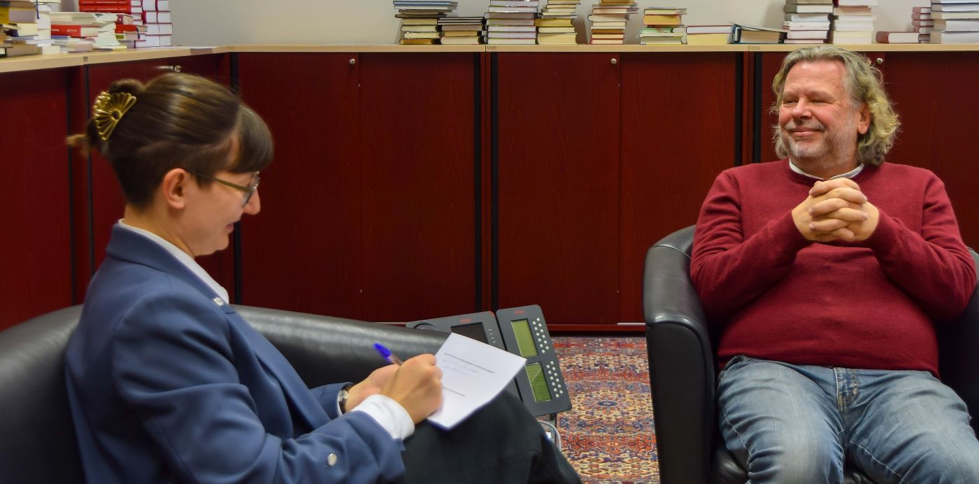 Lena Sinzinger, BA MA und Vizepräsident Dr. Michael Sachs sitzen auf zwei schwarzen Lederstühlen und unterhalten sich beim Interview. Im Hintergrund befinden sich Holzkästen und viele Bücher.